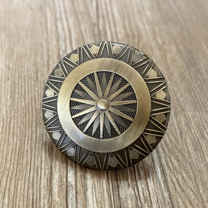 Peut inclure: Un bouton de porte rond en laiton avec un motif géométrique. Le bouton a un motif central en étoile entouré d'un anneau de triangles.