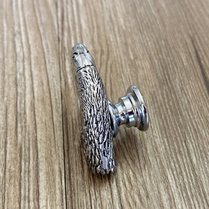 May include: A silver cabinet knob with a detailed animal design. The knob has a round base and a textured, animal-shaped handle.