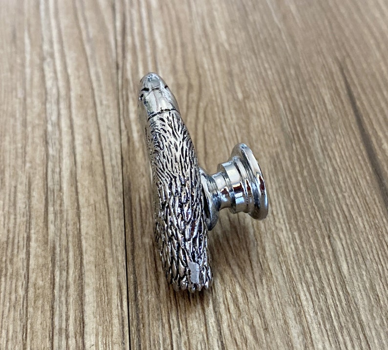 May include: A silver cabinet knob with a detailed animal design. The knob has a round base and a textured, animal-shaped handle.