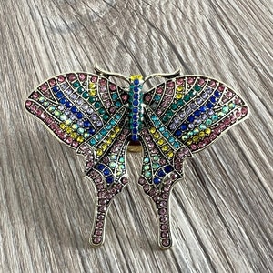 May include: A colourful butterfly brooch with pink, blue, green and yellow rhinestones. The butterfly is made of metal and has a detailed design.