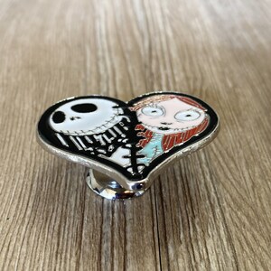 May include: A black and white heart-shaped metal cabinet knob with a cartoon image of Jack Skellington and Sally from the Nightmare Before Christmas movie.