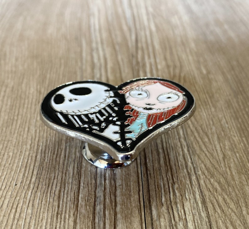 May include: A black and white heart-shaped metal cabinet knob with a cartoon image of Jack Skellington and Sally from the Nightmare Before Christmas movie.