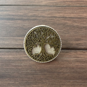 May include: A round, silver and bronze pendant with a tree of life design. The tree is intricately detailed with branches and leaves.