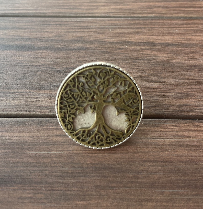 May include: A round, silver and bronze pendant with a tree of life design. The tree is intricately detailed with branches and leaves.