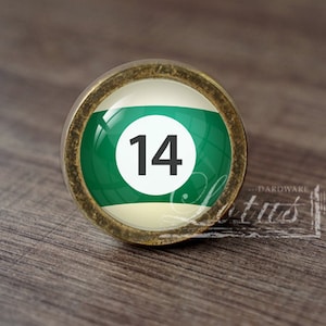 Op de afbeelding: Een groene en witte biljartbal met het nummer 14 erop. De bal zit in een gouden frame.