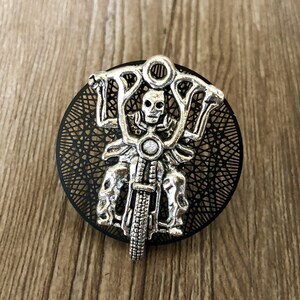 Op de afbeelding: Een zilverkleurige skeletmotorrijder-bedel met een zwarte filigraan achtergrond.