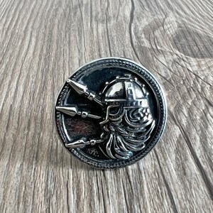 Op de afbeelding: Een zilverkleurige ring met een gedetailleerd ontwerp van een Viking-strijdershoofd met een helm en omringd door drie speren.
