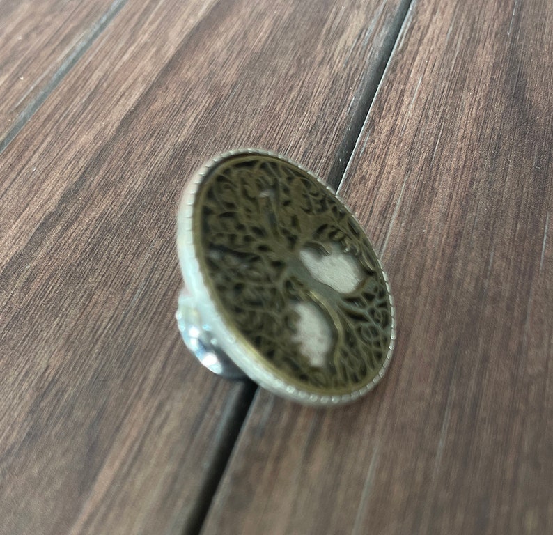 May include: A silver and gold metal pendant featuring a tree of life design. The pendant is round and has a detailed, intricate design.