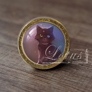 May include: A gold-toned round cabinet knob with a glass insert featuring a black cat with one yellow eye and one blue eye. The cat is looking directly at the viewer.