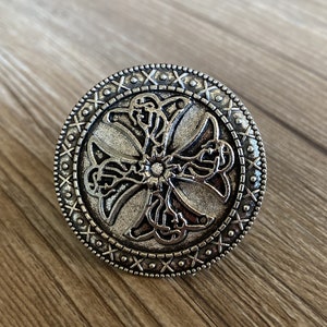 May include: A silver-toned metal ring featuring a Celtic cross design. The cross is encircled by a decorative border of dots and X's.