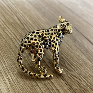 Peut inclure: Une broche dor&eacute;e en forme de l&eacute;opard avec des taches noires. Le l&eacute;opard a les yeux verts et un design d&eacute;taill&eacute;.