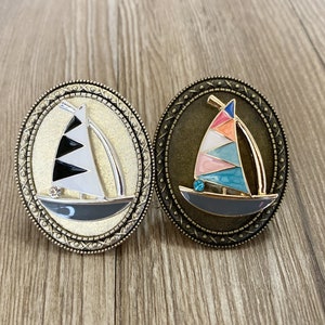 May include: Two decorative sailboats with a gold trim and a jeweled accent. The sailboats are on a round, bronze-coloured base with a decorative pattern.