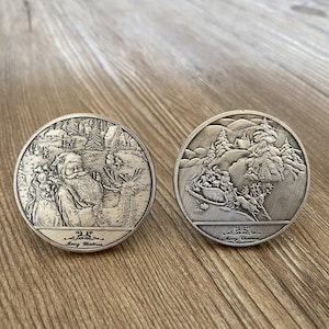 May include: Two silver-toned round Christmas ornaments with raised images. One ornament features Santa Claus with a reindeer, and the other features a sleigh pulled by reindeer. Both ornaments have the text "Merry Christmas" inscribed on them.