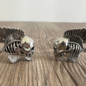 May include: Two silver skeleton fish with skull heads. The fish are facing opposite directions and have detailed skeletal features.