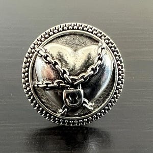 Könnte beinhalten: Ein silberner Ring mit einem Herzdesign. Das Herz ist von einer Kette und einem Vorhängeschloss umgeben.