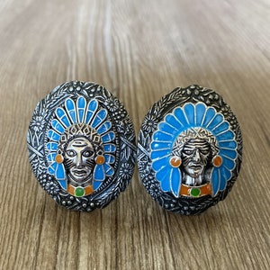 Könnte beinhalten: Zwei silberne Ringe mit blauen und orangefarbenen Emaille-Designs. Jeder Ring zeigt einen indianischen Häuptling mit einem Federkopfschmuck.
