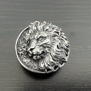 Peut inclure: Un pendentif en argent repr&eacute;sentant une t&ecirc;te de lion avec un design d&eacute;taill&eacute;. La crini&egrave;re du lion est flottante et la t&ecirc;te est tourn&eacute;e vers la droite.