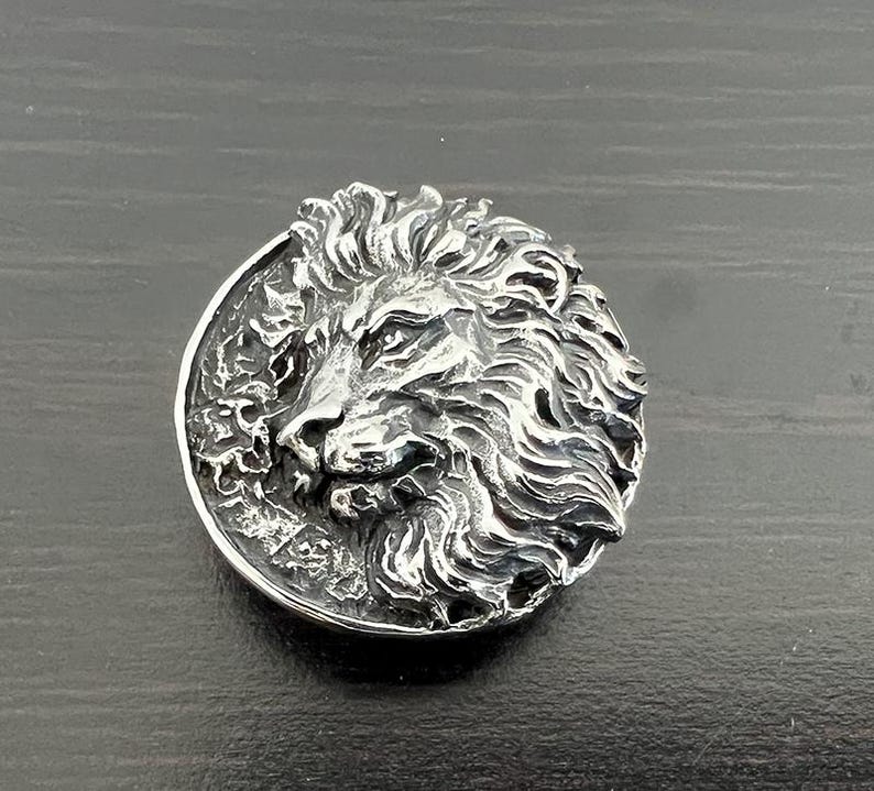 Peut inclure: Un pendentif en argent repr&eacute;sentant une t&ecirc;te de lion avec un design d&eacute;taill&eacute;. La crini&egrave;re du lion est flottante et la t&ecirc;te est tourn&eacute;e vers la droite.