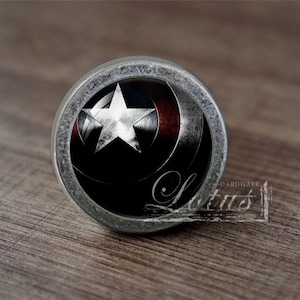 Könnte beinhalten: Ein runder, silberfarbener Schrank-Knopf mit einem schwarzen und roten Bild von Captain Americas Schild. Der Schild hat einen weißen Stern in der Mitte.