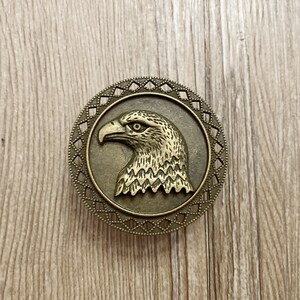 May include: A bronze eagle head ornament with a detailed design, set in a circular frame with a decorative border.