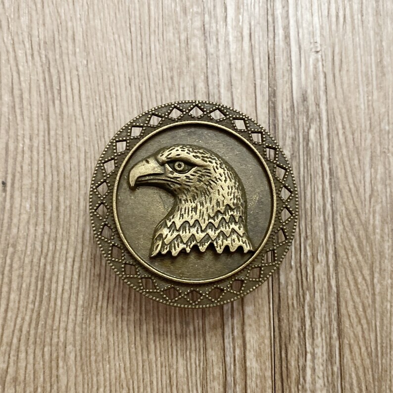 May include: A bronze eagle head ornament with a detailed design, set in a circular frame with a decorative border.