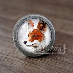 May include: A silver knob with a glass insert featuring a detailed illustration of a fox's face. The fox has white fur with orange markings around its eyes and nose.