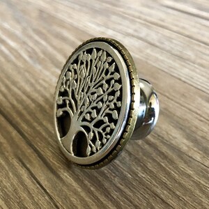 May include: A silver and gold tree of life design bottle stopper. The stopper is round and has a detailed tree design with leaves and branches.