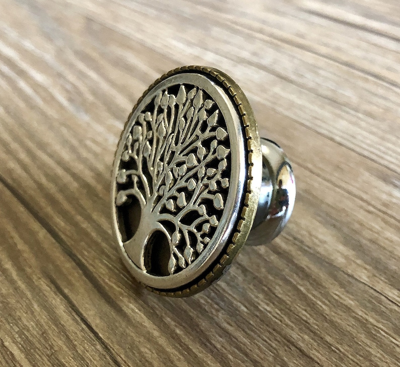 May include: A silver and gold tree of life design bottle stopper. The stopper is round and has a detailed tree design with leaves and branches.