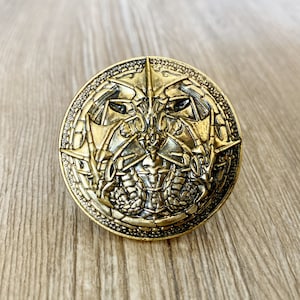 May include: A gold-toned metal pin with a detailed design of three dragons facing each other. The dragons have intricate scales and wings.