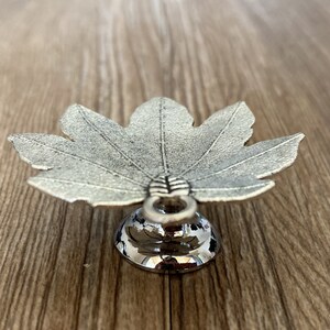 Pode incluir: Um prato de prata em forma de folha com uma base redonda. O prato &eacute; feito de metal e tem um acabamento brilhante.