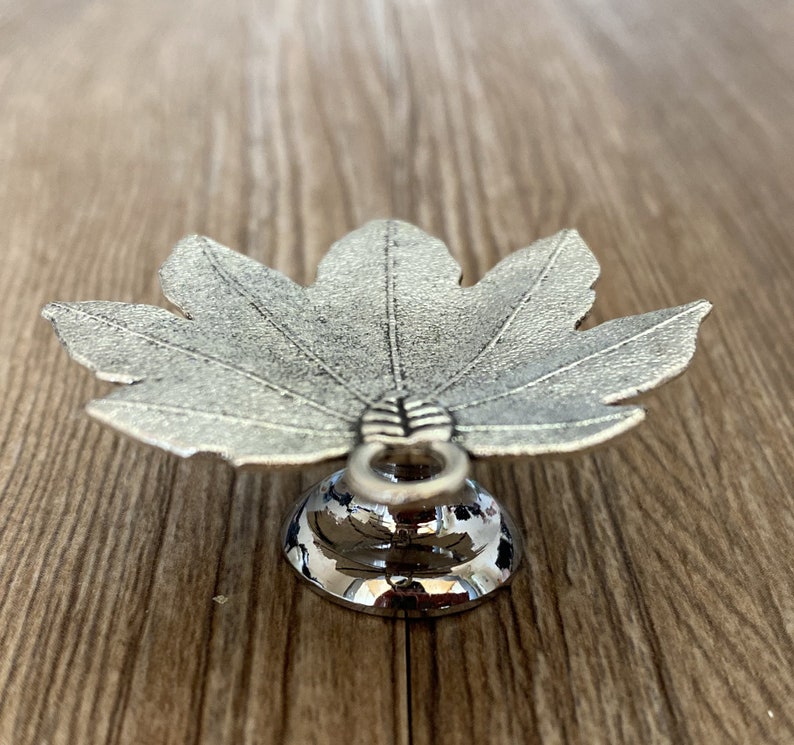 Pode incluir: Um prato de prata em forma de folha com uma base redonda. O prato &eacute; feito de metal e tem um acabamento brilhante.