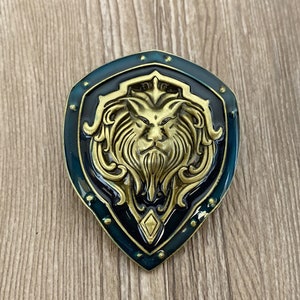 Könnte beinhalten: Ein dunkelgrüner Schild mit einem goldenen Löwenkopfdesign. Der Löwe hat eine detaillierte Mähne und einen grimmigen Ausdruck.