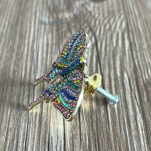 May include: A gold butterfly-shaped cabinet knob with a colourful mosaic design. The knob has a screw for attaching it to a cabinet door.