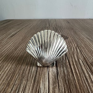 May include: A silver seashell shaped dish, sitting on a wooden surface.