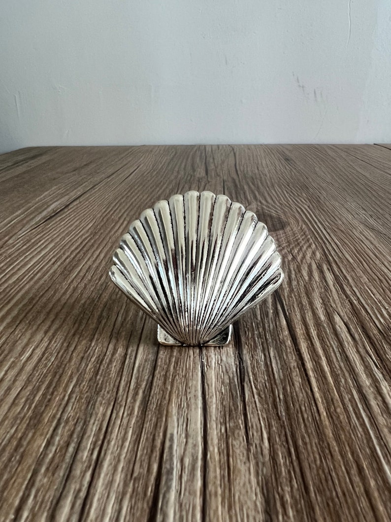 May include: A silver seashell shaped dish, sitting on a wooden surface.