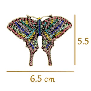 May include: A colourful butterfly brooch with a gold finish and rhinestones. The brooch measures 6.5 cm wide and 5.5 cm tall.