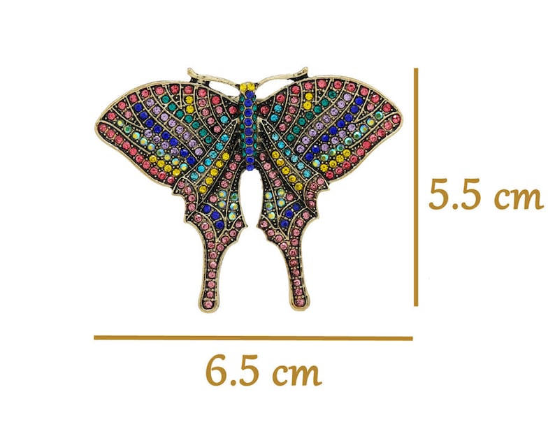 May include: A colourful butterfly brooch with a gold finish and rhinestones. The brooch measures 6.5 cm wide and 5.5 cm tall.