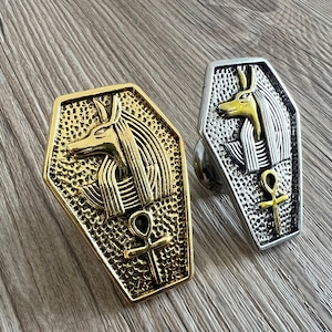 May include: Two coffin-shaped cabinet knobs with an Egyptian Anubis jackal design. One knob is gold and the other is silver.