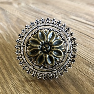 May include: A silver and bronze ring featuring a floral design. The ring is circular with a detailed filigree pattern.