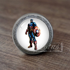 Op de afbeelding: Een zilveren knop met een ronde, witte voorkant met een cartoon afbeelding van Captain America in zijn kenmerkende rood-wit-blauwe kostuum, met zijn schild.