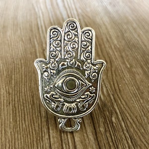 May include: Silver-toned metal hamsa hand charm with an ornate design and a blue eye in the centre.