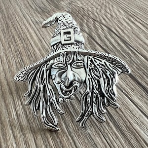 Op de afbeelding: Een zilverkleurig heksenbeeldje met een puntige hoed en een gedetailleerd gezicht. De heks heeft lang, golvend haar en een ondeugende uitdrukking.