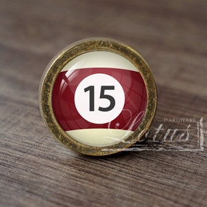 May include: A gold-toned cabinet knob featuring a red and white billiard ball design. The ball has the number "15" printed in black.