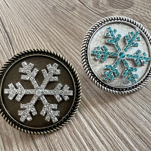 May include: Two decorative snowflake ornaments with a silver and bronze finish. The snowflakes are made of metal and have a raised design with rhinestones.