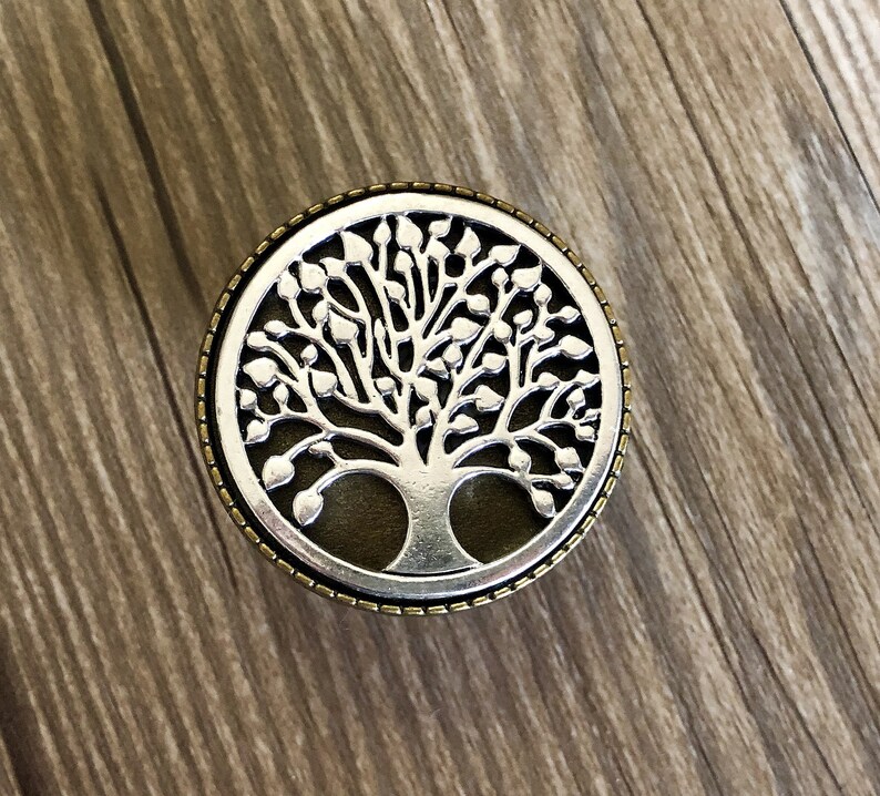 May include: A silver tree of life design with a dark brown background, surrounded by a gold-colored border.