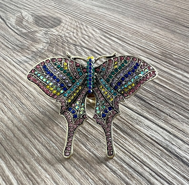 May include: A colourful butterfly ring with rhinestones in shades of pink, blue, green, and yellow.
