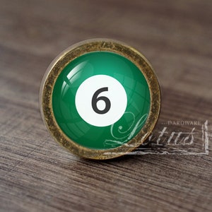 May include: A round cabinet knob with a green and gold finish, featuring a white billiard ball design with the number "6".