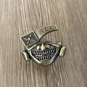 May include: A gold-toned metal door handle with a grinning face and the text "東京喰種" in Japanese characters.