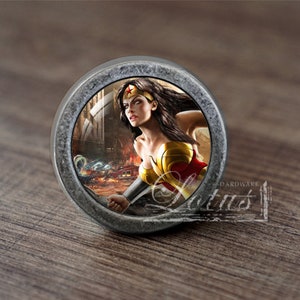 Könnte beinhalten: Ein runder, silberfarbener Schrank-Knopf mit einem detaillierten Bild von Wonder Woman in einer Kampfszene. Das Bild ist von einem silberfarbenen Rand umgeben.