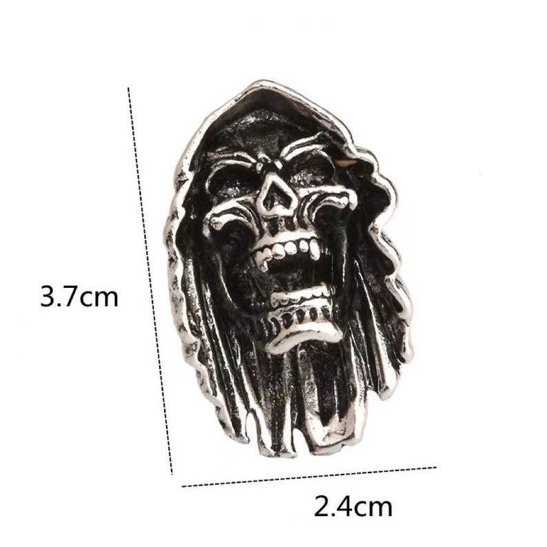 Op de afbeelding: Een zilverkleurige schedelring met een ontwerp van een Grim Reaper. De ring is 3,7 cm hoog en 2,4 cm breed. De schedel heeft een open mond en draagt een kap. De ring is waarschijnlijk gemaakt van metaal.